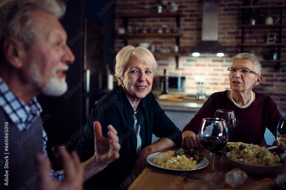 Senior friend group having wine and dinner at home together