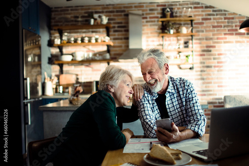 Senior couple using a smartphone while going over financials in the kitchen
