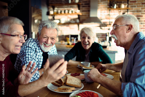 Group of senior friends using a smartphone while having breakfast together in the kitchen