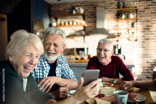 Group of senior friends using a smartphone while having breakfast together in the kitchen