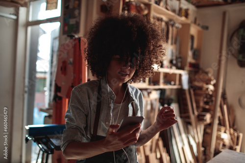 Young mixed woman listening to music on his smartphone in a carpenters garage