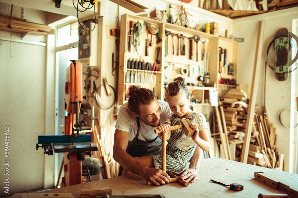 Young carpenter father teaching his daughter how to assemble wood in the garage - obrazy, fototapety, plakaty 