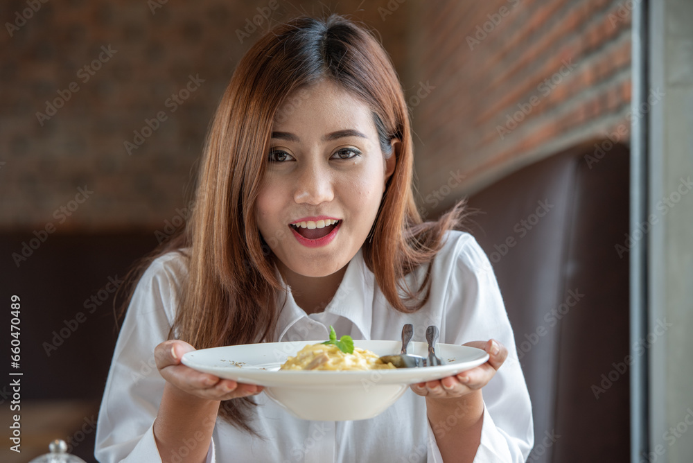 Woman in white clothes holding and smell white dish plate with pasta homemade spaghetti marinara in restaurant background. Lady smell and eat pasta spaghetti by fork.