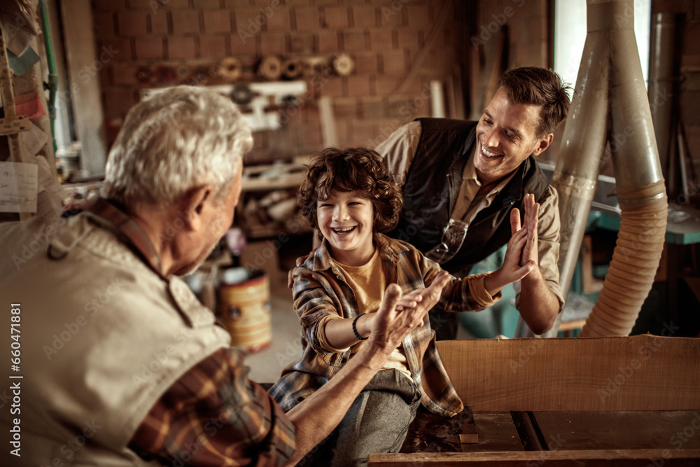Multigenerational family of male carpenters high fiving each other in a carpentry shop