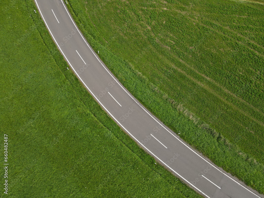Drone view of a curved asphalt road between green grass fields in the landscape 