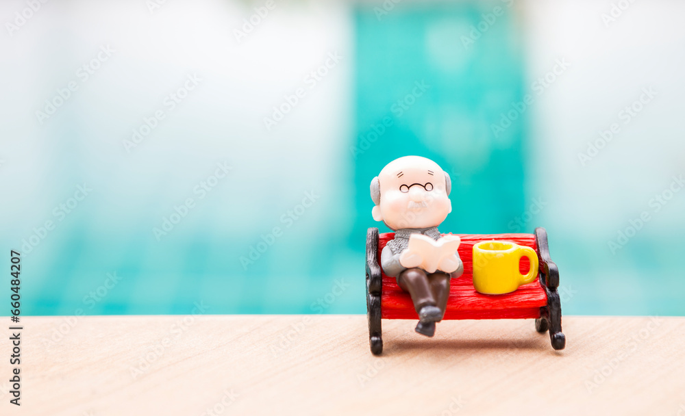 Miniature old man sitting on red bench with tea cup on swimming pool edge, outdoor day light, retirement life Miniature old man sitting on red bench with tea cup on swimming pool edge, outdoor day light, retirement life