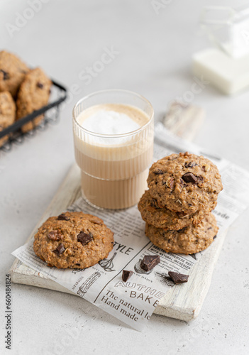 Stack of delicious freshly baked oatmeal cookies with nuts and chocolate drops and a glass of latte on a light background. Snack, breakfast concept. Healthy oat biscuits with chocolate recipe photo