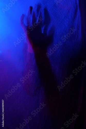 Arms of woman pressing against curtain. silhouette woman behind blue light poses mysteriously and artistically