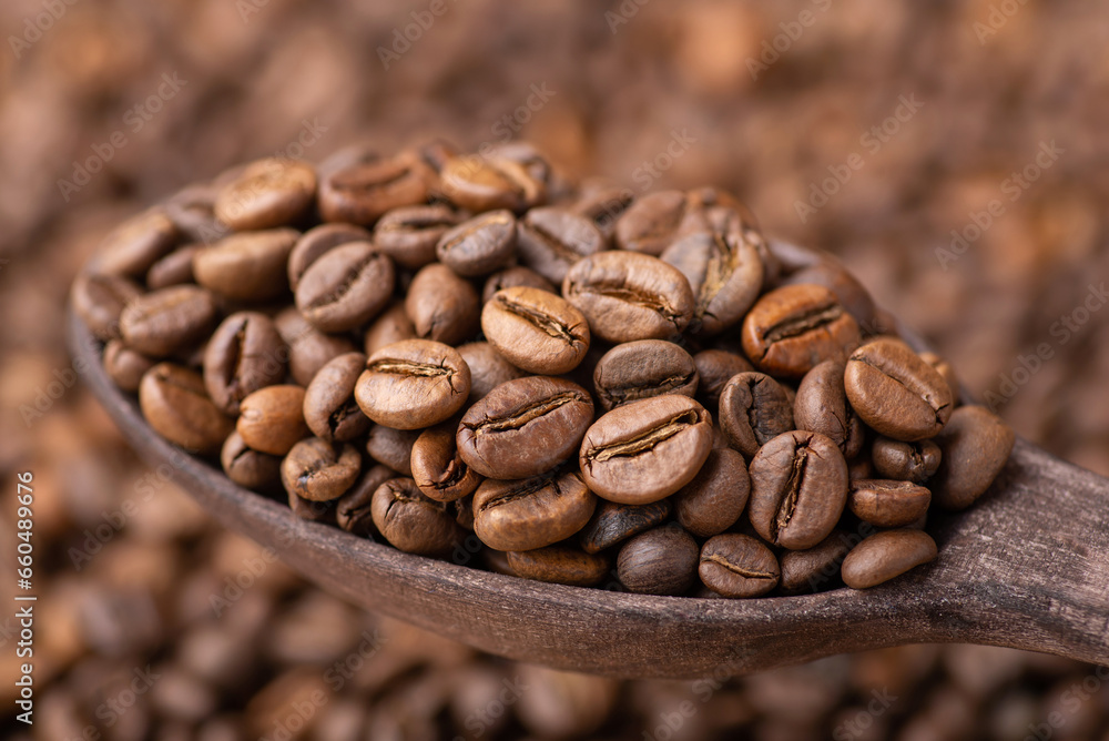 Dark roasted coffee beans in wooden spoon. Background of fresh roasted coffee grain