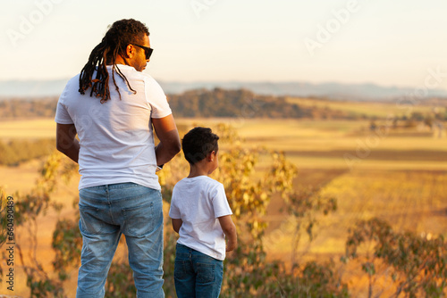 Aboriginal father and son standing on edge of cliff looking out over country landscape photo