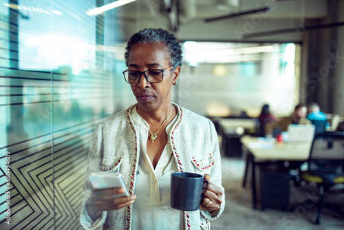 Senior African American businesswoman using her smartphone on a coffee break in the modern office