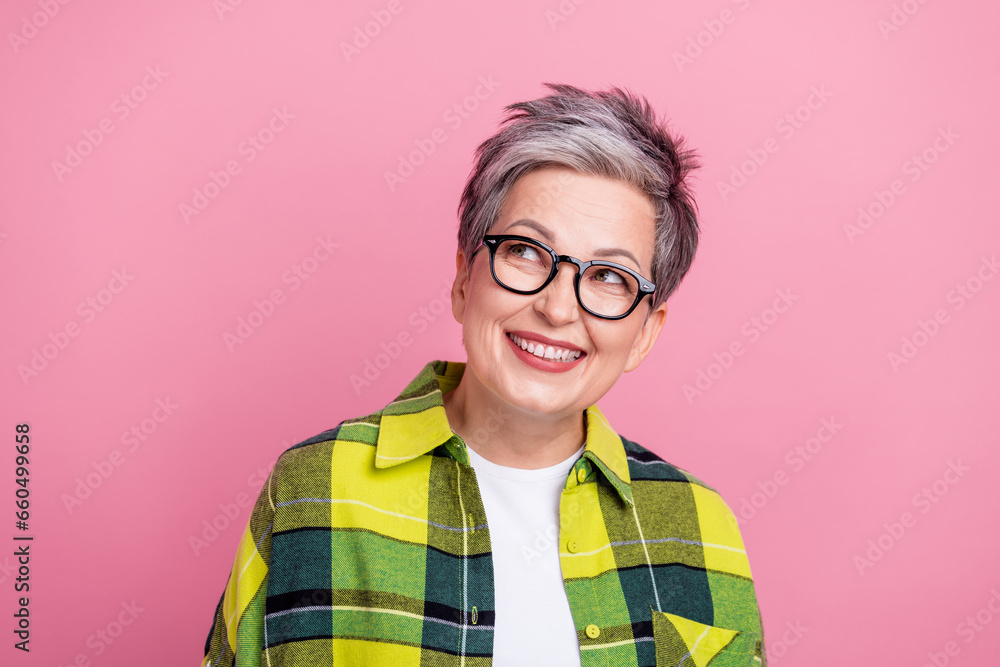 Photo of good mood retired woman with short hairstyle wear checkered shirt look at offer empty space isolated on pink color background