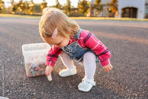 Toddler girl drawing with chalk on quiet suburban road photo