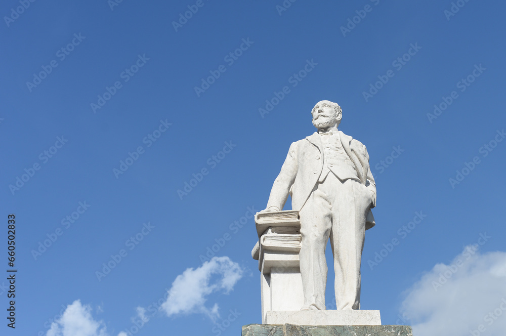 White stone statue of Mario Cermenati, a local scientist and politician, in Lecco, Lake Como, Italy. With blue sky and white fluffy cloud