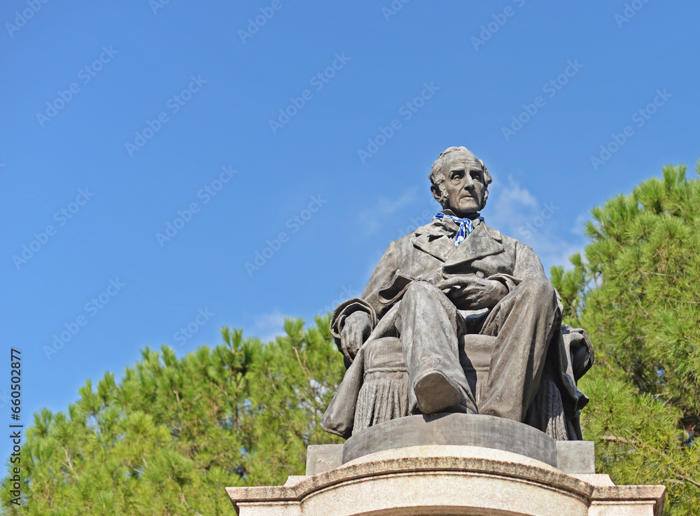 Statue of Alessandro Manzoni, an Italian writer and poet, in Lecco, Lake Como, Italy. With blue sky and green tree. Selective focus