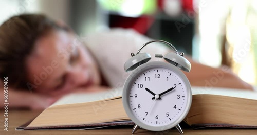 Alarm clock on open book woman lies and sleeps on table. Overstudy and insomnia and overwork photo