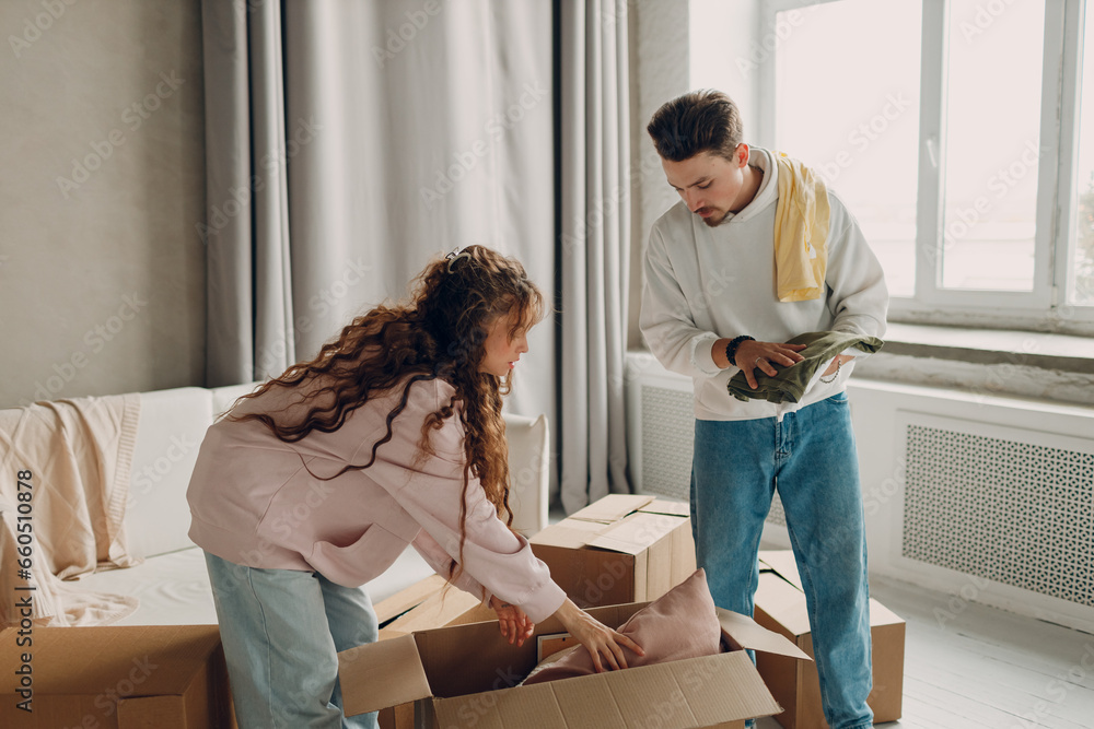Happy young family couple man and woman unpacking box after moving cardboard boxes to new home apartment. Happy young family couple man and woman unpacking box after moving cardboard boxes to new home apartment.