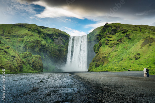 Powerful Skogafoss waterfall flowing with couple tourist enjoying in summer at Iceland