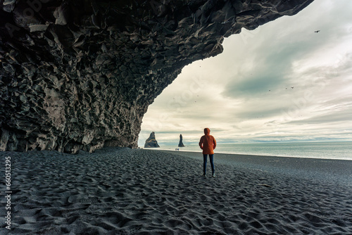 Reynisdrangar natural rock formation with female tourist standing in halsanefshellir cave on black sand beach in summer at Iceland
