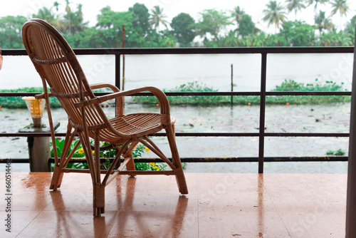 An empty cane chair overlooking the backwater in Allepey, Kerala during a rainy day in the monsoon season from a balcony near the waterfront in a luxury resort