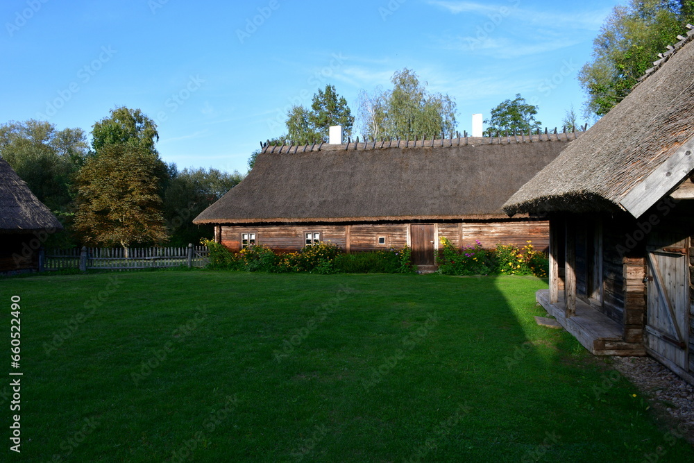 A view of an old wooden hut, shack, or stable surrounded with growing flowers, herbs, a wooden fence, and ancient farming equipment seen next to a well maintained lawn, pastureland, or meadow A view of an old wooden hut, shack, or stable surrounded with growing flowers, herbs, a wooden fence, and ancient farming equipment seen next to a well maintained lawn, pastureland, or meadow