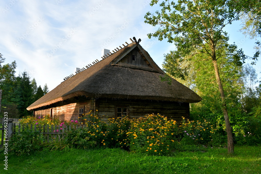 A view of an old wooden hut, shack, or stable surrounded with growing flowers, herbs, a wooden fence, and ancient farming equipment seen next to a well maintained lawn, pastureland, or meadow A view of an old wooden hut, shack, or stable surrounded with growing flowers, herbs, a wooden fence, and ancient farming equipment seen next to a well maintained lawn, pastureland, or meadow