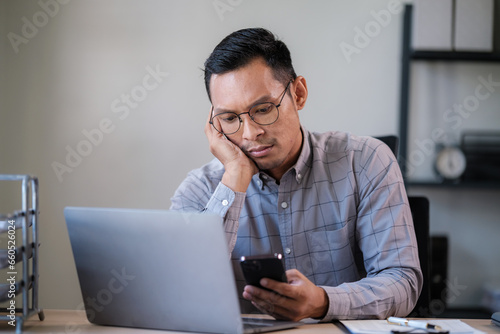 Freelance business man calling on mobile smartphone while working with laptop seriously stress depression, businessman mobile phone calling with customers. Smart phone conversation conference.
