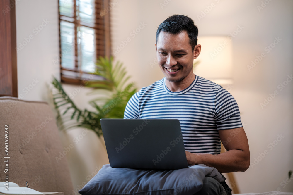Serious young eastern man working on laptop while sitting on sofa at home Serious young eastern man working on laptop while sitting on sofa at home