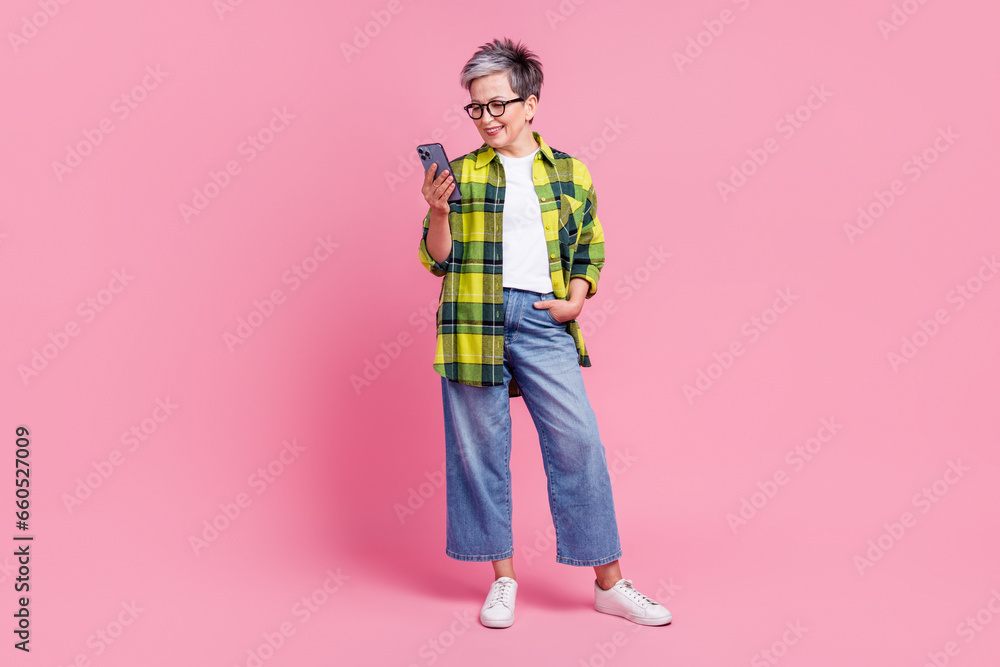 Full size photo of intelligent person with gray hair dressed plaid shirt look at smartphone read email isolated on pink color background Full size photo of intelligent person with gray hair dressed plaid shirt look at smartphone read email isolated on pink color background