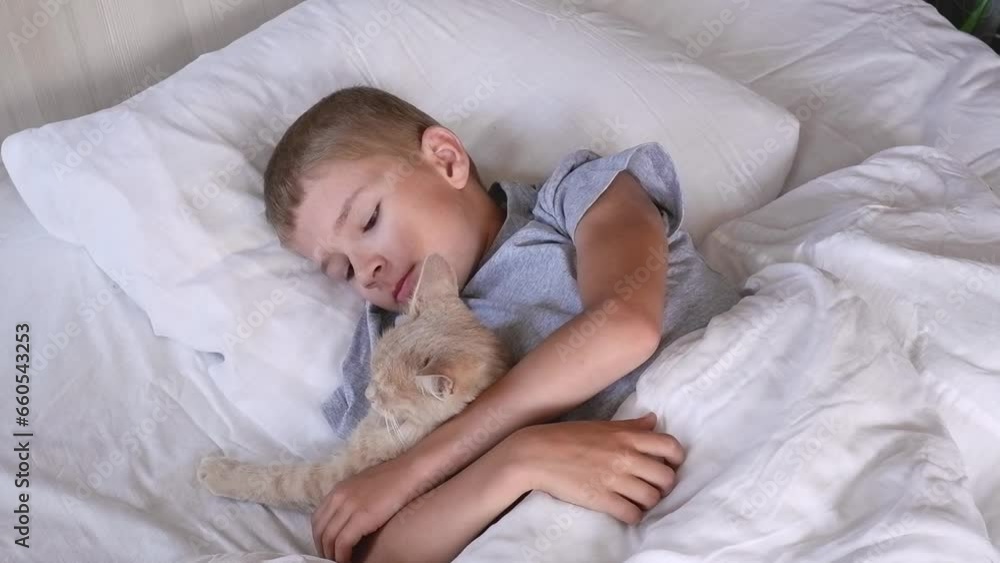 The child does not sleep in the bed, but plays with the red cat. Friendship of children with animals. The child does not sleep in the bed, but plays with the red cat. Friendship of children with animals.