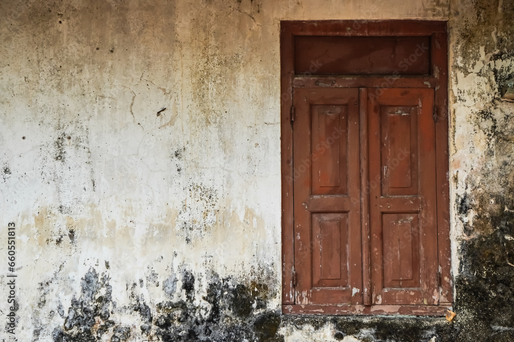Closed old Javanese wooden window with shutters on an moldy white concrete wall. Concept for traditional exterior, vintage, heritage, rural housing ornament. Empty blank copy text space. Omah Joglo