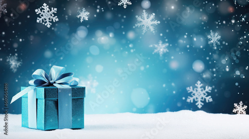 Blue gift box with a bow on a snowy surface with falling snowflakes in the background. Free space for product placement or advertising text. © OleksandrZastrozhnov