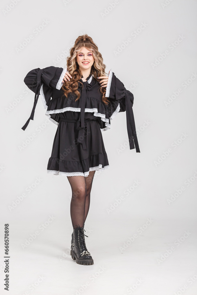 young girl in black school dress poses as doll on white background in studio young girl in black school dress poses as doll on white background in studio