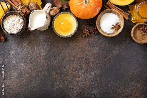 Homemade fall baking background with ingredients pumpkins, sugar, flour, nuts, eggs and spices on a dark stone table.
