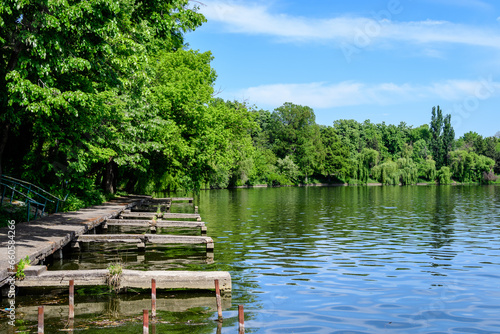 Landscape with white boat on Herastrau lake and large green trees in King Michael I Park (Herastrau) in Bucharest, Romania, in a sunny spring day.