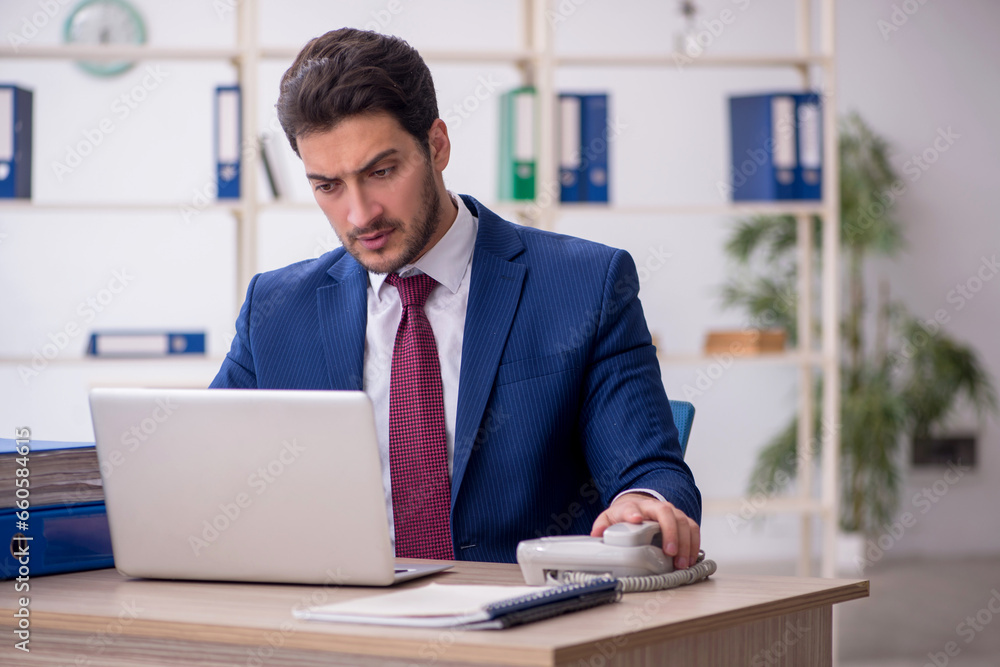 Young male employee speaking by phone in the office Young male employee speaking by phone in the office
