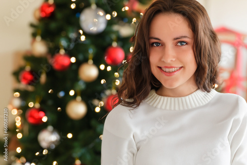 Christmas portrait of a beautiful brunette woman with a wide smile against the background of a Christmas tree