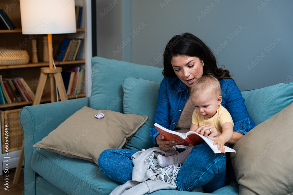 Mom reading a book with baby boy or girl at home. Early age children education, development. Mother and child spending time together read fairy tales on sofa in evening. Parent love concept