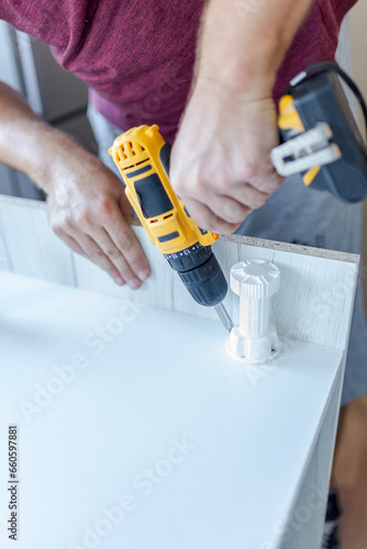 Furniture assembler man holding screwdriver for assembling kitchen wooden rack and attaching legs