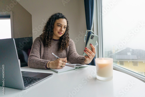 Curly hair young woman working on laptop in cozy nook with mug	