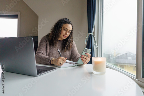 Curly hair young woman working on laptop in cozy nook with mug	