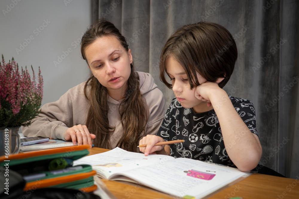 Mom watches as her child does her homework. Mom studies with her son at home. Home schooling. Mom watches as her child does her homework. Mom studies with her son at home. Home schooling.