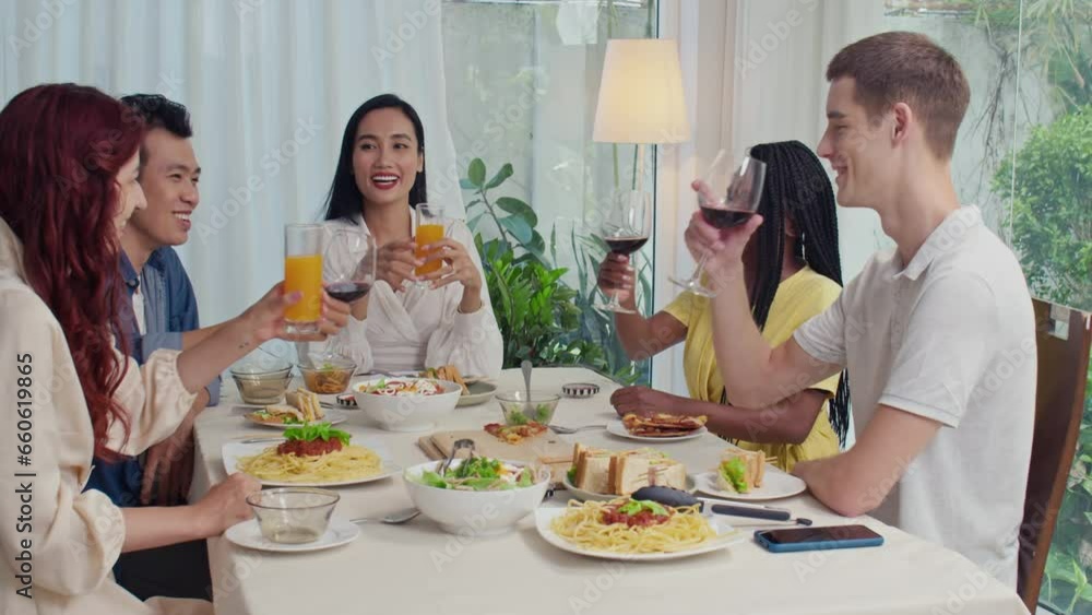 Group of multicultural friends clinking glasses with red wine and orange juice while celebrating at festive table at home Group of multicultural friends clinking glasses with red wine and orange juice while celebrating at festive table at home