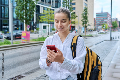 Portrait of young teenage female student with smartphone, on street of city