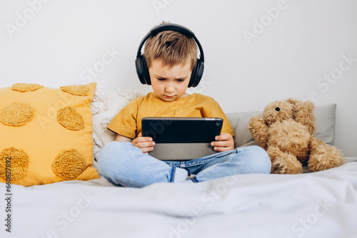 Toddler boy playing with digital wireless tablet computer at home. Baby child growing with online applications. Child and electronic devices concept. Portrait of toddler with smartphone