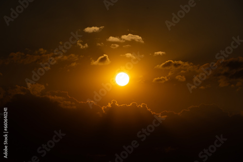 The sun setting among the clouds. Orange saturated sunset. Sun rays reflecting from delicate clouds.