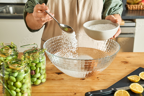 Woman preparing canning brine for fermented olives using antic recipe of measuring out salt needed using water and egg. Autumn vegetables canning. Healthy homemade food. Conservation of harvest. photo