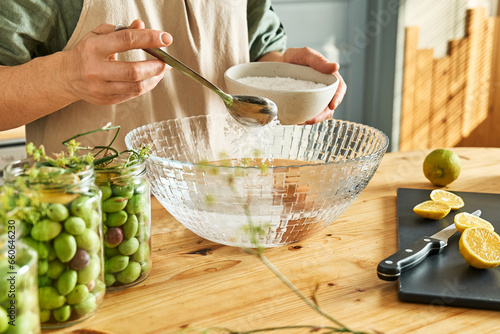 Fotografie Woman preparing canning brine for fermented olives using antic recipe of measuring out salt needed using water and egg