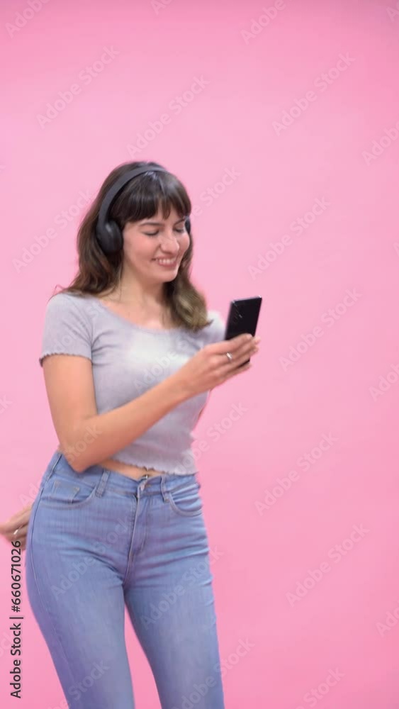 A beautiful young woman wearing headphones dances to music on a smartphone A beautiful young woman wearing headphones dances to music on a smartphone