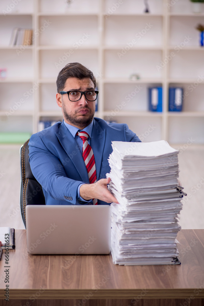 Young male employee unhappy with excessive work in the office Young male employee unhappy with excessive work in the office